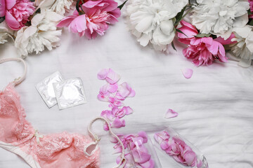 Fototapeta na wymiar omen's lace lingerie on a white bed. Tulips, perfume, lipstick, condoms. Woman devices. Date. Romantic day. Flat lay with copy space