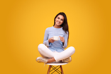 Smiling Hispanic lady drinking coffee in bright yellow studio