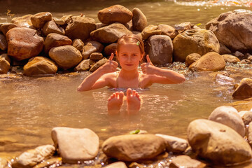 Young beautiful child girl enjoy of water in wild lake near waterfall in the forest. Horizontal image.