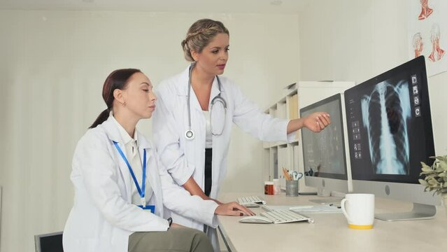 Female doctor explaining chest x ray image on computer screen with colleague while working together in clinic