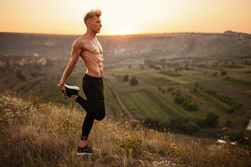 Fit confident sportsman stretching legs on hill slope during outdoor training