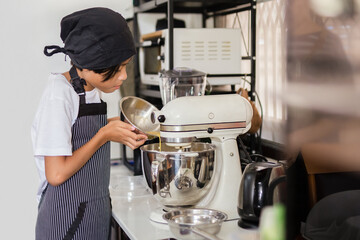 Young boy pouring egg yolk into electric mixer bowl.