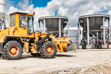 A large front loader transports materials in a concrete production plant. Production of concrete. Transportation of bulk materials. Construction equipment. Bulk cargo transportation.