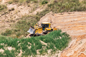 A powerful bulldozer in a sand pit is planning a site. Extraction of sand in an open pit. natural building materials.