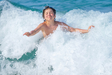 joyful boy bathes in sea waves on Cleopatra beach, Alanya, Antalya, Turkey