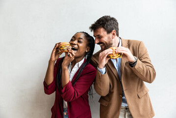 Two young business people or smart casual white man and African American woman holding and eating...