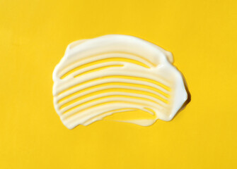 The texture of white cream on yellow background. A smear of moisturizer closeup. Lotion swatch. Beauty, skin care product smear smudge drop. SPF sunscreen cream sample