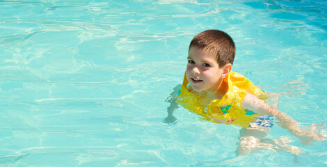 A 5-year-old boy is learning to swim in an inflatable vest in a pool, a place for text.