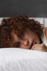 Beautiful girl with curly red hair on the bed in the morning 