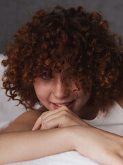 Beautiful girl with curly red hair on the bed in the morning 