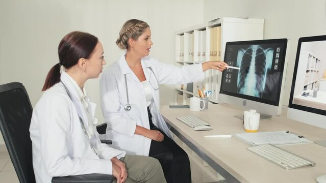 Two professional female doctors discussing chest x ray image on computer while working together in clinic