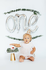 Fototapeta Beautiful photo session set up for baby girl celebrating one year old birthday on white background. Delicious biscuit cake with butter cream and candle one obraz