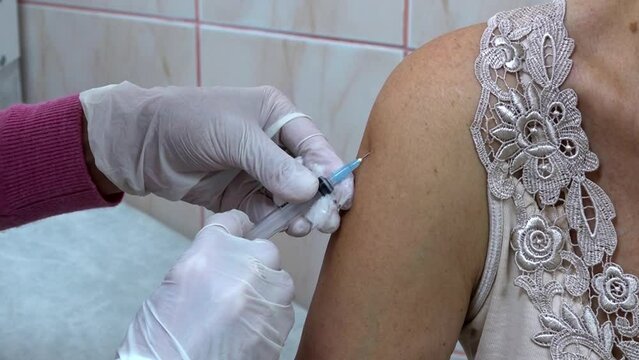 Adult female patient receives a vaccine injection in a hospital, close-up. Stimulation of immunity to minimize the risk of contracting a pandemic. The doctor injects the flu vaccine into the arm.