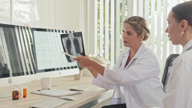 Female doctor holding chest x ray scan and discussing it with colleague while working in clinic