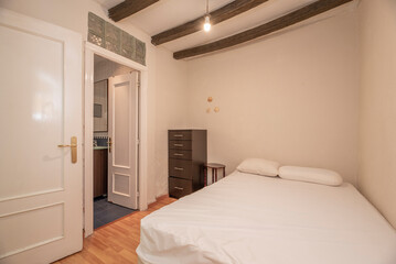 Small bedroom with exposed beams, queen trundle bed, brown chest of drawers, access to a bathroom and wooden floor