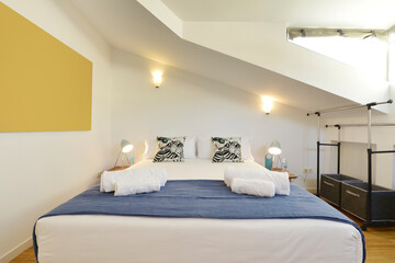 Bedroom with a double bed in an attic room, blue details, white cushions and black and white cushions, skylights, oak parquet flooring and a clothes rack