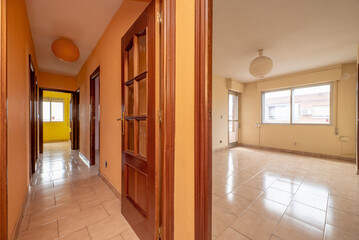 Corridor of a house with reddish wood doors, light stoneware floors and aluminum windows