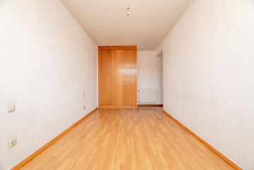 Fototapeta na wymiar Empty room with white walls, a light wooden floor, a built-in wardrobe with three wooden doors and a white aluminum radiator