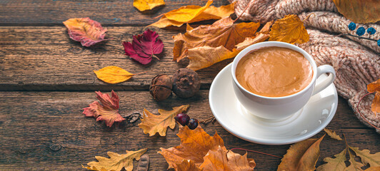 Coffee mug and autumn foliage on a wooden background. Cozy autumn composition. Side view, copy space