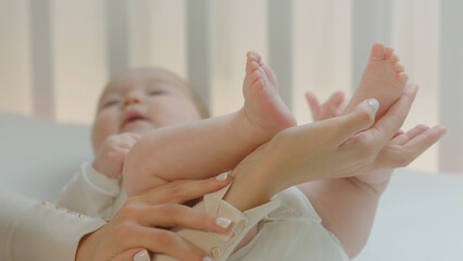 Closeup to the camera smiling large young mother with passion kissing her baby s legs and smiling large in the morning routine