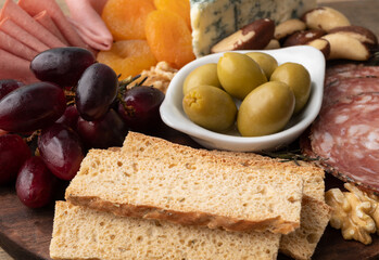 Appetizer board with cheese, nuts, fruits, toasts and charcuterie over wooden table