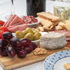 Appetizer board with cheese, nuts, fruits, toasts, wine and charcuterie over wooden table