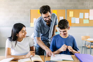 Male teacher helping high school students doing exercises in classroom - Education and college people concept - Powered by Adobe