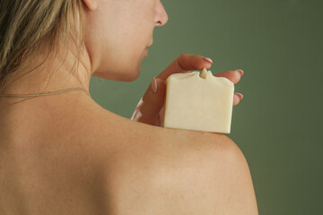 Young Caucasian woman holding soap bar on her shoulder. Natural handmade organic skin care cosmetic.