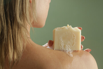 Young Caucasian woman holding soap bar on her shoulder. Natural handmade organic skin care cosmetic. - obrazy, fototapety, plakaty