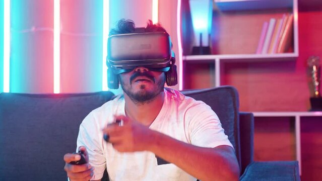 Focus on VR, Young gamer playing video game on virtual reality or VR headset using joystick at home - concept of metaverse, cyberspace and futuristic.
