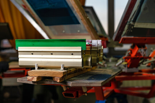 serigraphy production. squeegees on wooden shelve of the print screening apparatus. printing images on t-shirts by silk screen method in a design studio