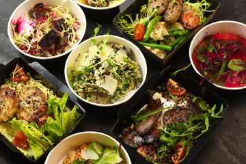 Delivery of healthy food in takeaway restaurants for daily nutrition. Set of containers with everyday meals - meat, fish, vegetables and law fat snacks on a black background.