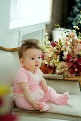 A little girl sitting on a vintage sofa in pink clothes.