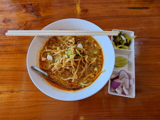 Khao Soi Recipe, Northern Style Curried Noodle Soup with Chicken (or pork). Flat yellow noodles garnished with crispy fried thin noodles served with sliced ​​shallots,sour pickled vegetables, and lime