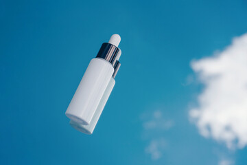 White bottle mockup with pipette for serum with hyaluron, collagen on blue sky background with clouds.