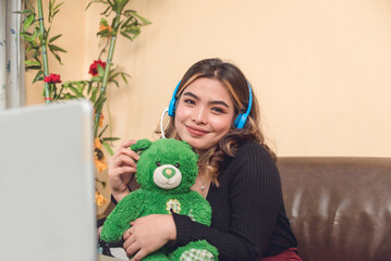 Pretty vlogger with blue headset posing with a cute green Teddy Bear plush toy. Blends perfectly well to the plain background