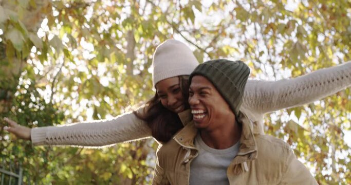 Loving, playful and happy couple having a piggyback and enjoying a fun date and walk through the park during autumn. Cheerful boyfriend laughing while giving his girlfriend a piggyback ride outdoors
