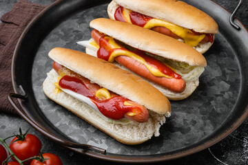 Hot dogs with ketchup, yellow mustard, on black dark stone table background