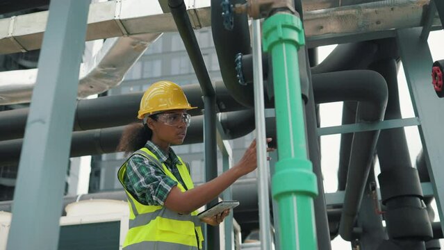 Professional engineer black women working checking and maintenance pipeline construction top of the building. Worker in safety uniform using tablet at pipeline construction system