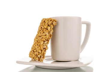One sweet roasted candy from sunflower seeds and honey on a white saucer with a cup, close-up, isolated on a white background.