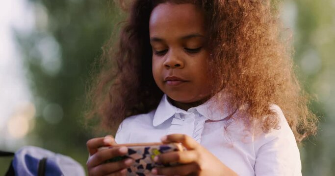 Teenage african american girl in school clothes with a smartphone plays a game application after studying at school