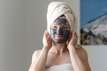 Woman removing facial dried clay mud mask with sponge in bathroom in front of mirror. Skin care....