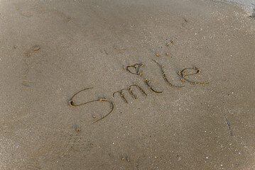 Smile message handwritten on the beach sand.