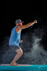 A man on a sub board with an oar in his hands on a black background in the fog.