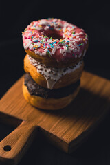 Delicious donuts on wooden board, placed on wooden cutting board on black background