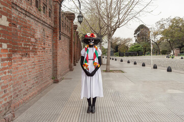 Front view of a woman standing with her hands in front of her and a costume and make-up of Catrina