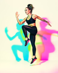 Fototapeta na wymiar Sporty girl jumping up. Photo of muscular woman in black sportswear on white background with effect of rgb colors shadows. Dynamic movement. Sports motivation and healthy lifestyle