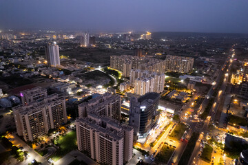 aerial drone shot showing brightly lit orange streets with skyscrapers, towers housing homes offices and shopping complexes in between with the city skyline in the distance in Gurgaon Delhi India
