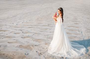 Fototapeta na wymiar Elegant girl in wedding dress posing in front of desert, sand, canyon with a bouquet in her hands