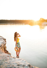 Young girl posing against the background of the sunset standing in the water, enjoying a summer trip to the lake.